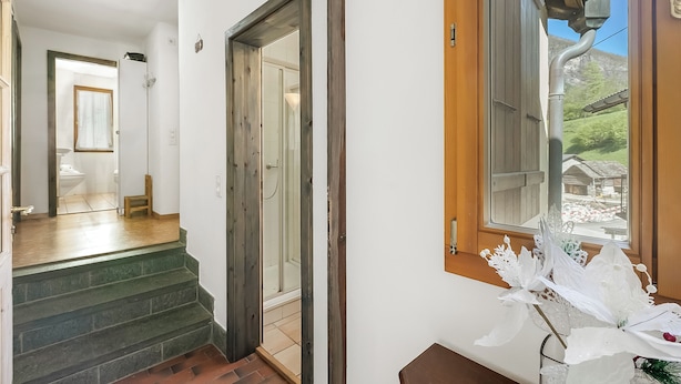 Una scala conduce a una stanza con una porta in legno, una finestra con vista su un edificio e un composizione floreale decorativa con fiori bianchi.