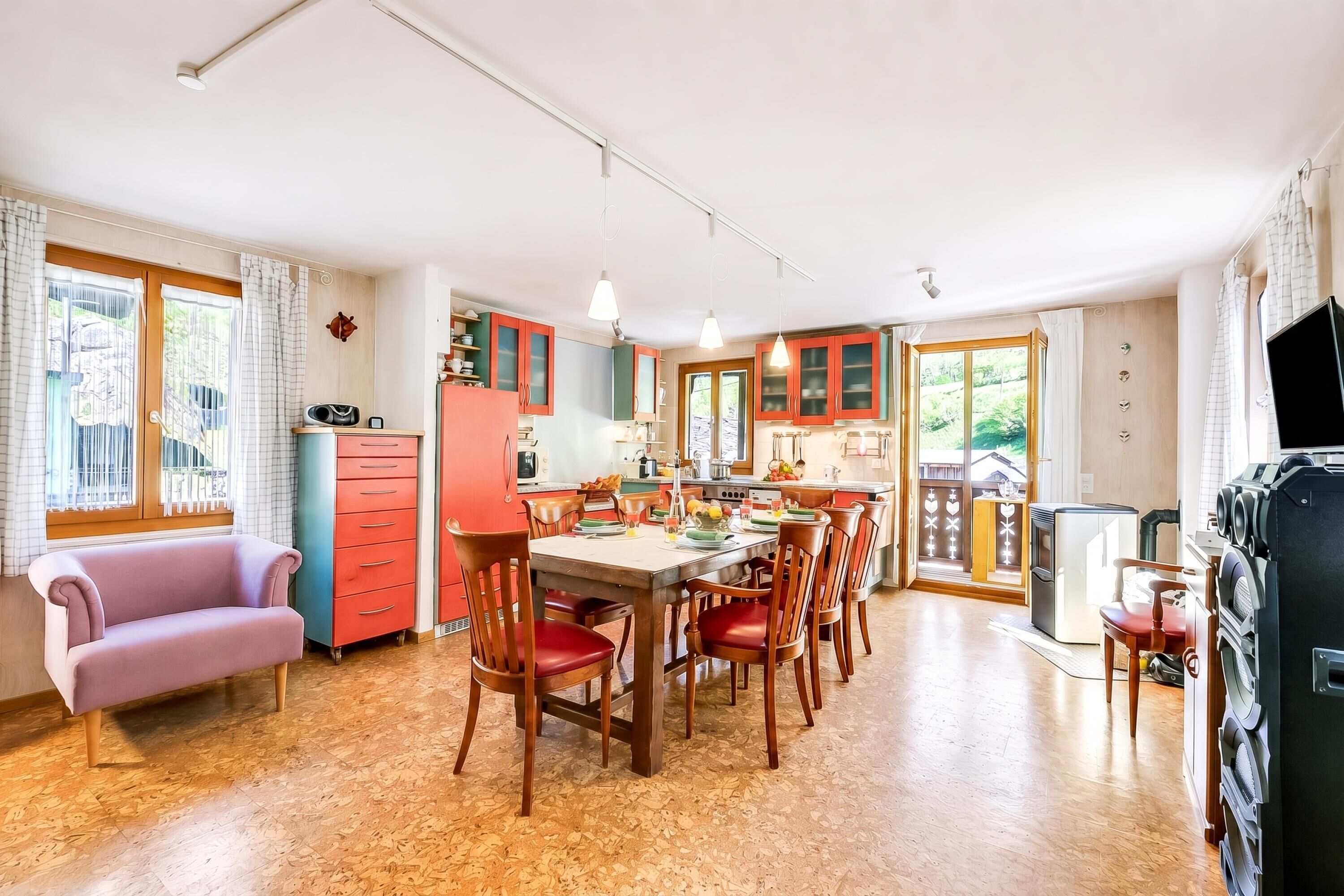 A spacious kitchen with wooden cabinets, a dining table with chairs, a sofa, and a television.