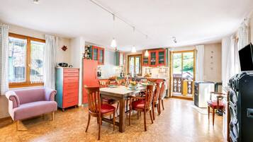 A spacious kitchen with wooden cabinets, a dining table with chairs, a sofa, and a television.