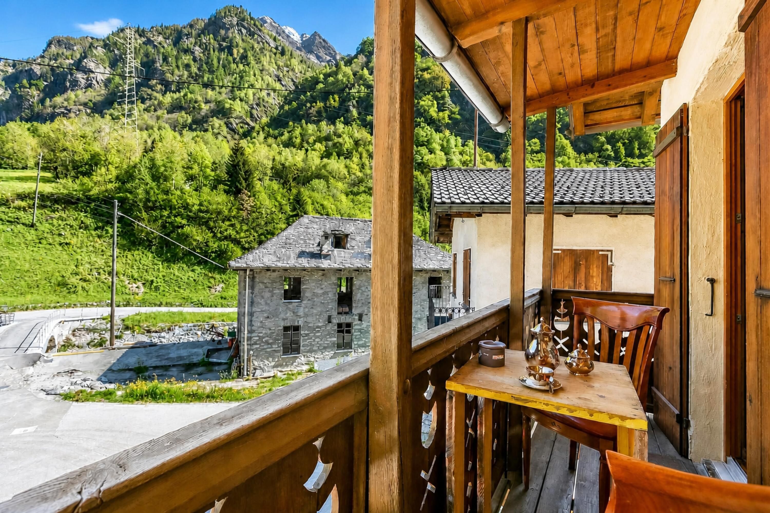 Un balcón de madera con una mesa y sillas, con vista a una montaña y un edificio pequeño.