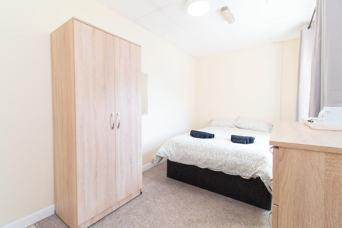 Quarto com uma cama, guarda-roupa e secretária.