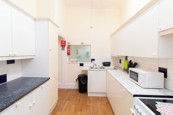 A compact kitchen with white cabinets, a microwave, a stove, and a sink.