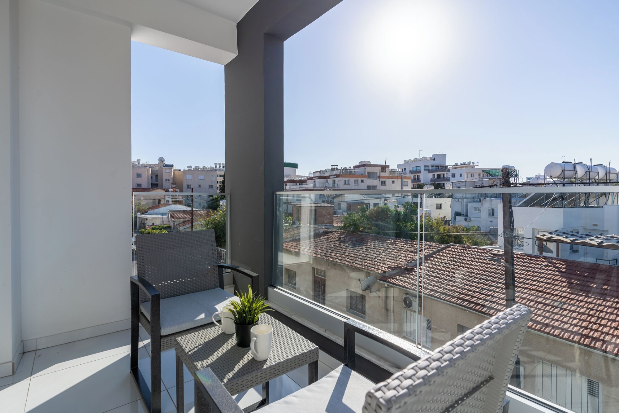 A balcony with a view of a cityscape, a potted plant, and a table with chairs.