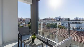 A balcony with a view of a cityscape, a potted plant, and a table with chairs.