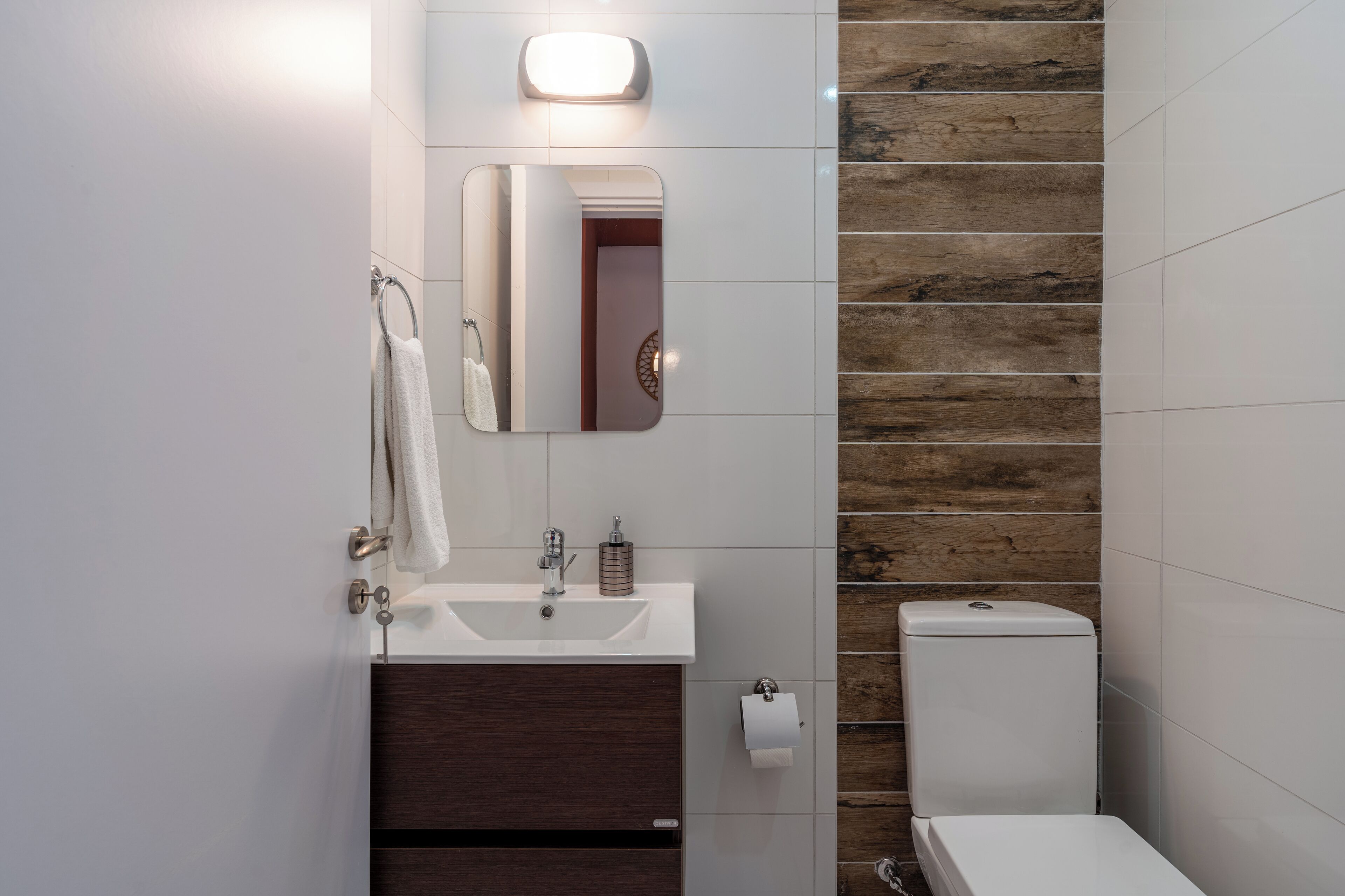 Un baño con lavamanos blanco, tocador de madera oscura, un espejo, inodoro y un panel de pared de madera.