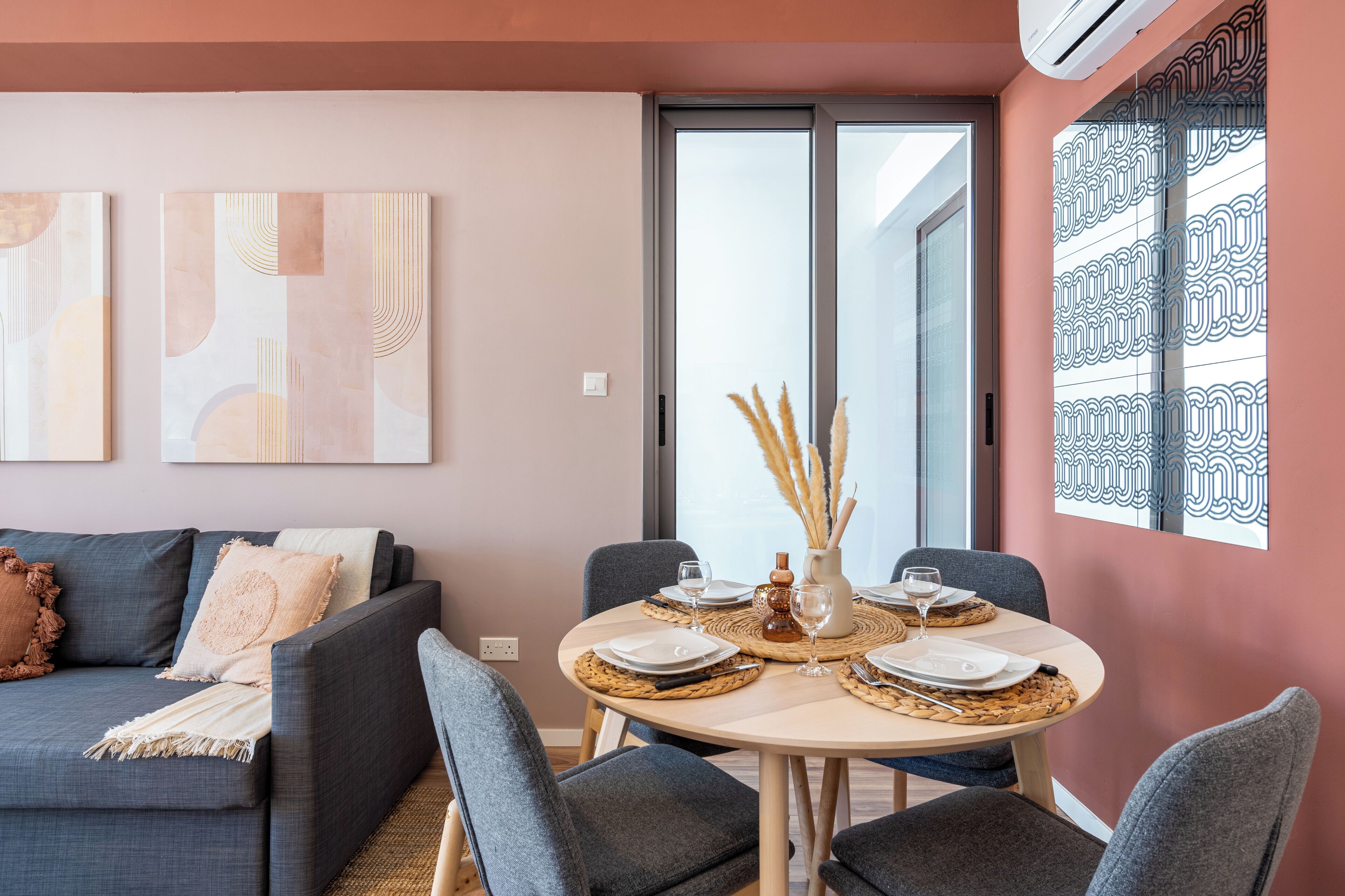 Un salon moderne avec un canapé gris, une table à manger ronde dressée pour quatre personnes et des œuvres d’art abstraites accrochées au mur.
