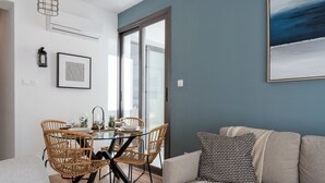 A dining area with wicker chairs, a glass table, and a framed picture on the wall. - Pauhad 3 - Larnaca Studios & Apts (Larnaca)