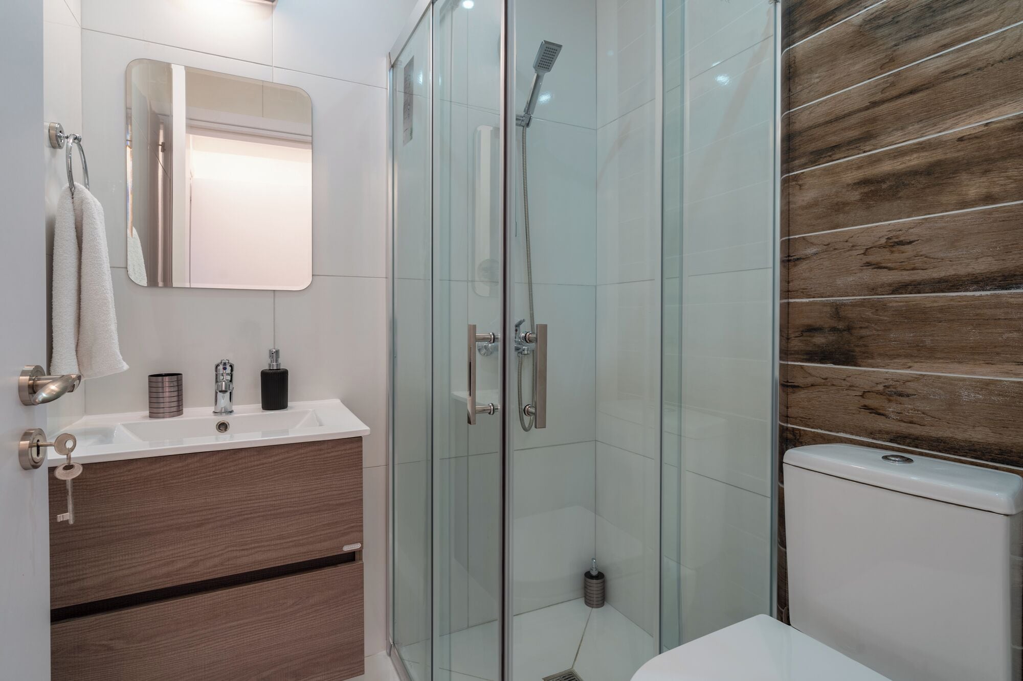 A modern bathroom with a glass shower enclosure, a wooden vanity, and a white sink.