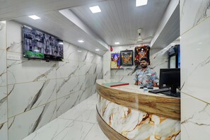 A reception area with a marble wall, a mounted television, and a wooden reception desk. - Hotel Lake Site (Mumbai)