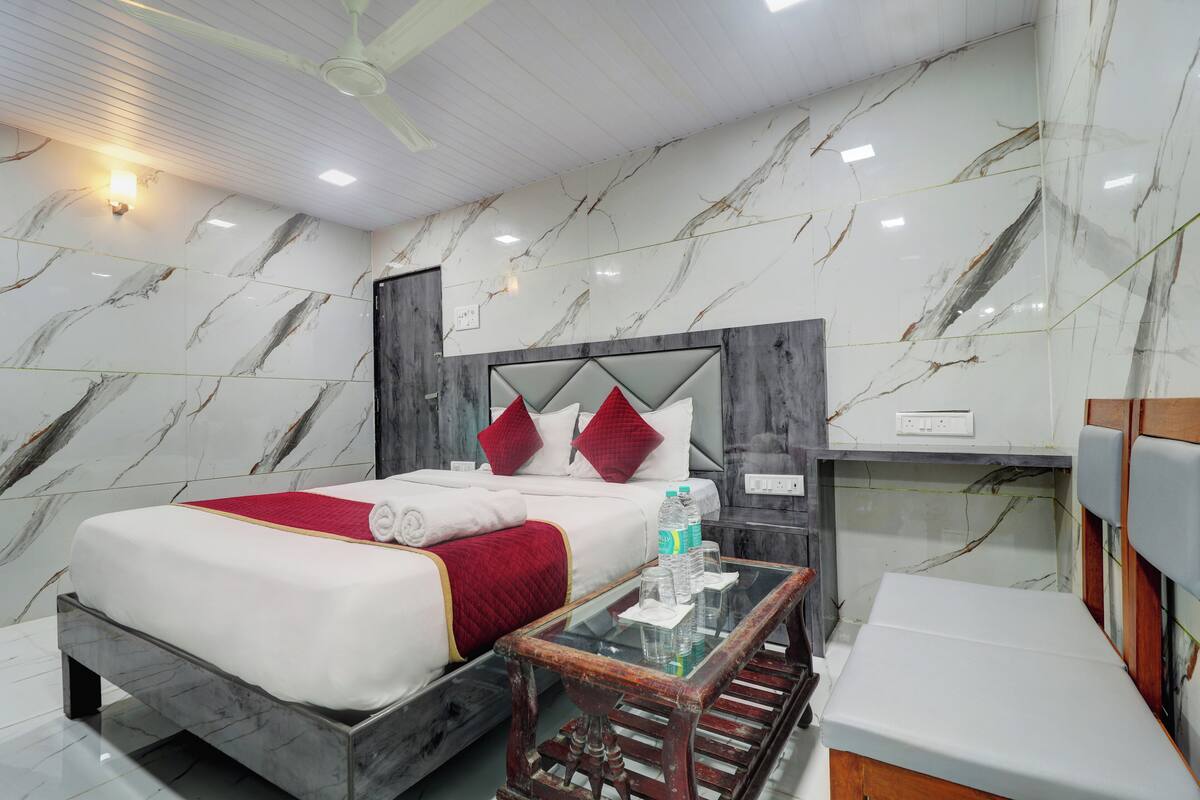 A hotel room with a marble-patterned wall, a bed with red and white bedding, a wooden nightstand, and a glass coffee table.