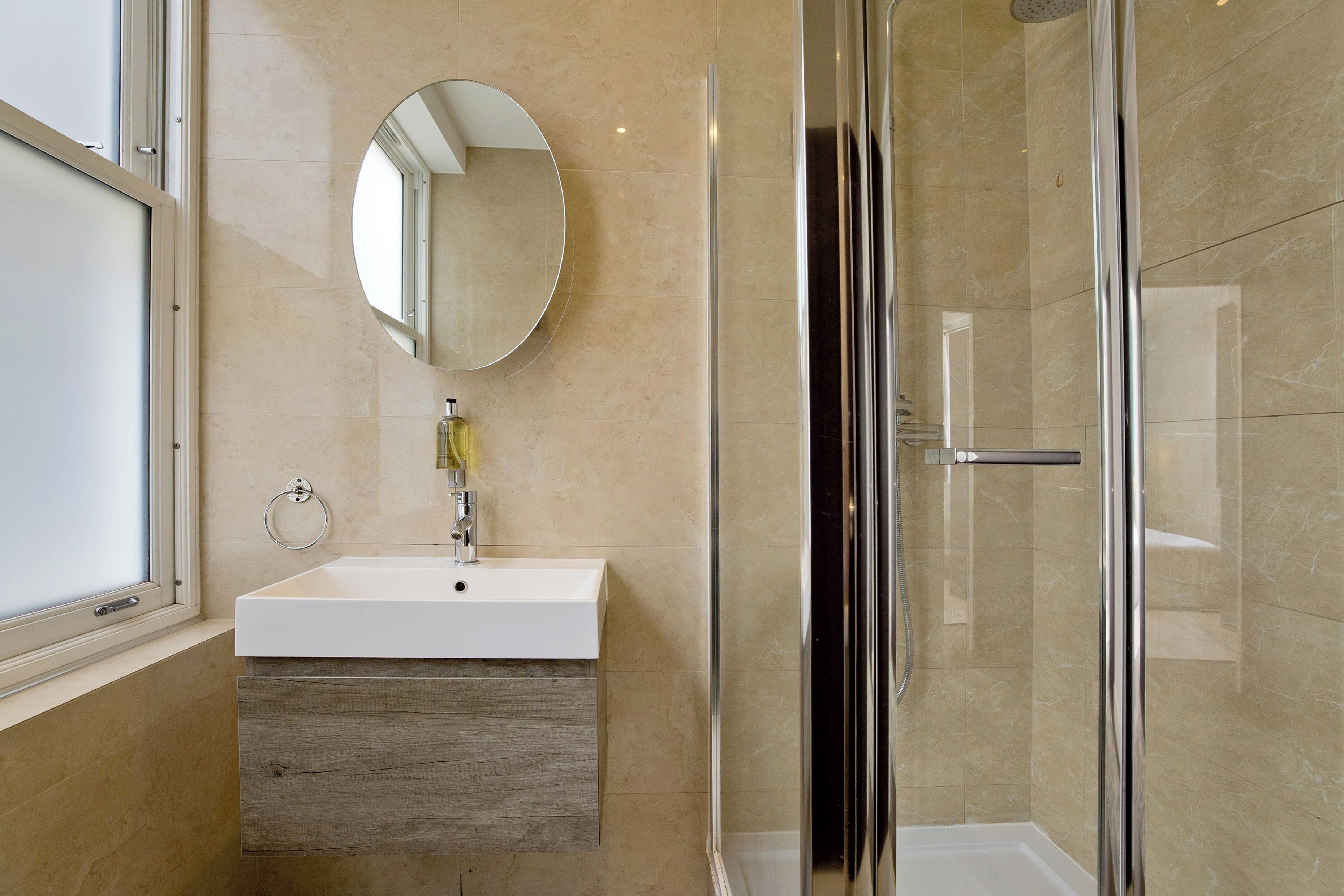A modern bathroom with a white sink, wooden vanity, a round mirror, and a glass shower enclosure.