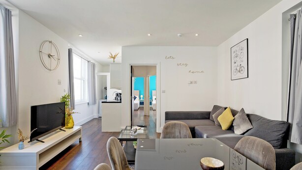 A modern living room with a flat-screen TV, a glass coffee table, and a sofa with cushions. - Imperial Middlesex Street Apartments (London)