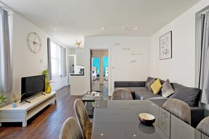 A modern living room with a flat-screen TV, a glass coffee table, and a sofa with cushions. - Imperial Middlesex Street Apartments (London)