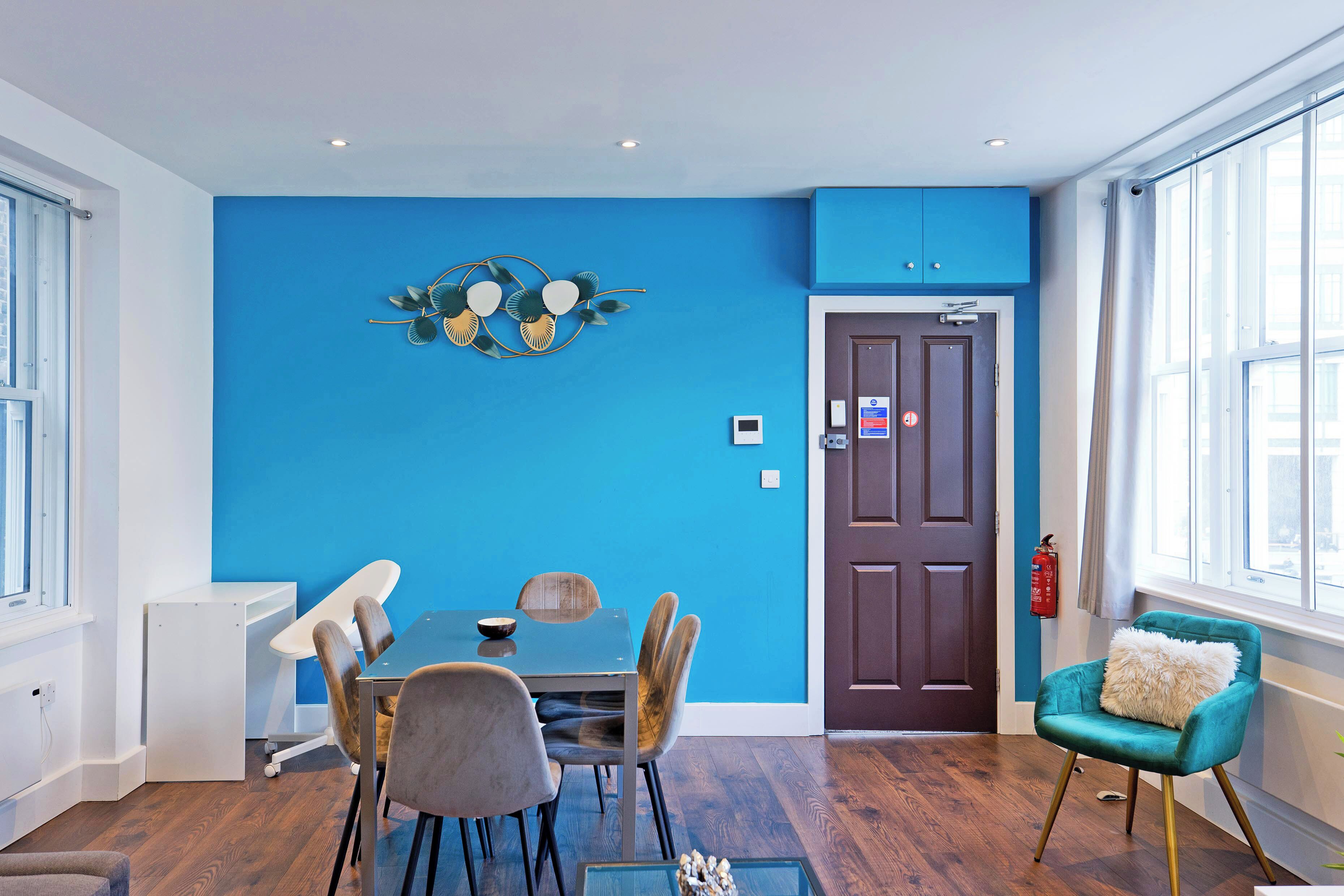 A modern dining area with a blue accent wall, a wooden dining table, and a teal armchair.