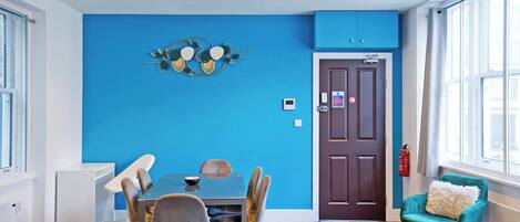 A modern dining area with a blue accent wall, a wooden dining table, and a teal armchair.
