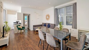 A modern living room with a glass dining table, grey sofas, and a kitchen area in the background. - Imperial Middlesex Street Apartments (London)