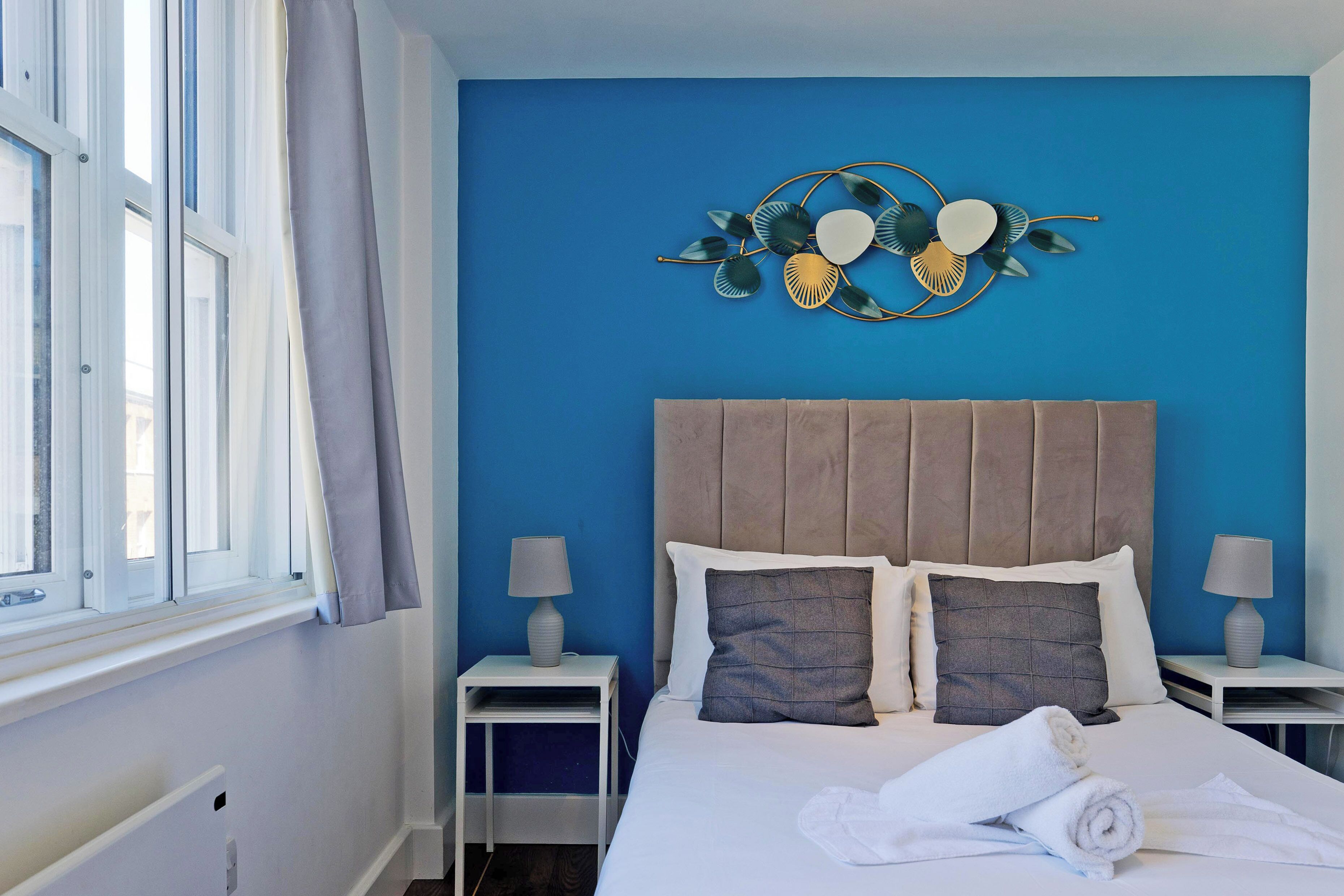 A neatly made bed with two pillows, a bedside table with a lamp, and a decorative wall piece.