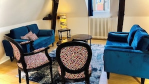 Una sala de estar acogedora con dos sofás azules, sillas estampadas, una mesita redonda y un radiador.