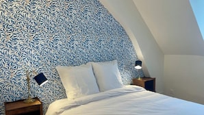 Un dormitorio con una cama blanca, dos mesitas de noche con lámparas y un papel tapiz estampado.