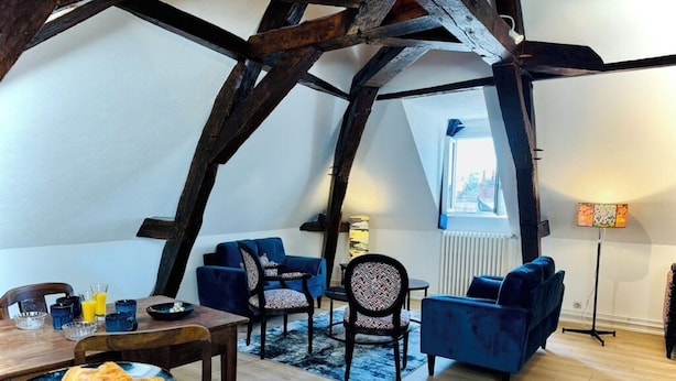 Un acogedor espacio tipo loft con vigas de madera a la vista, una zona de comedor con mesa dispuesta para el desayuno y un área de estar confortable con sofás y sillones.