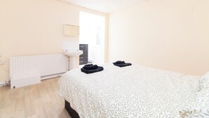 Ένα υπνοδωμάτιο με ένα κρεβάτι, ένα καλοριφέρ, έναν νιπτήρα και μια πόρτα που οδηγεί σε ένα μπάνιο.