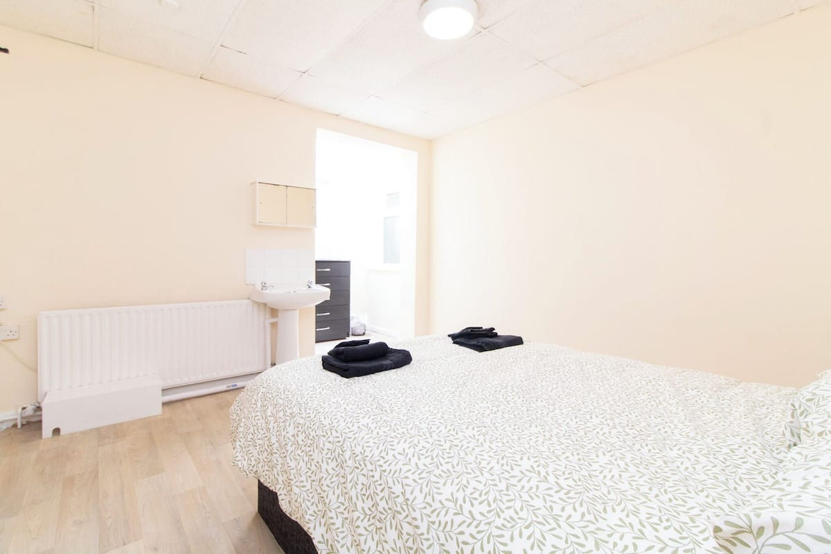 Un dormitorio con cama, radiador, lavabo y puerta que da a un baño.