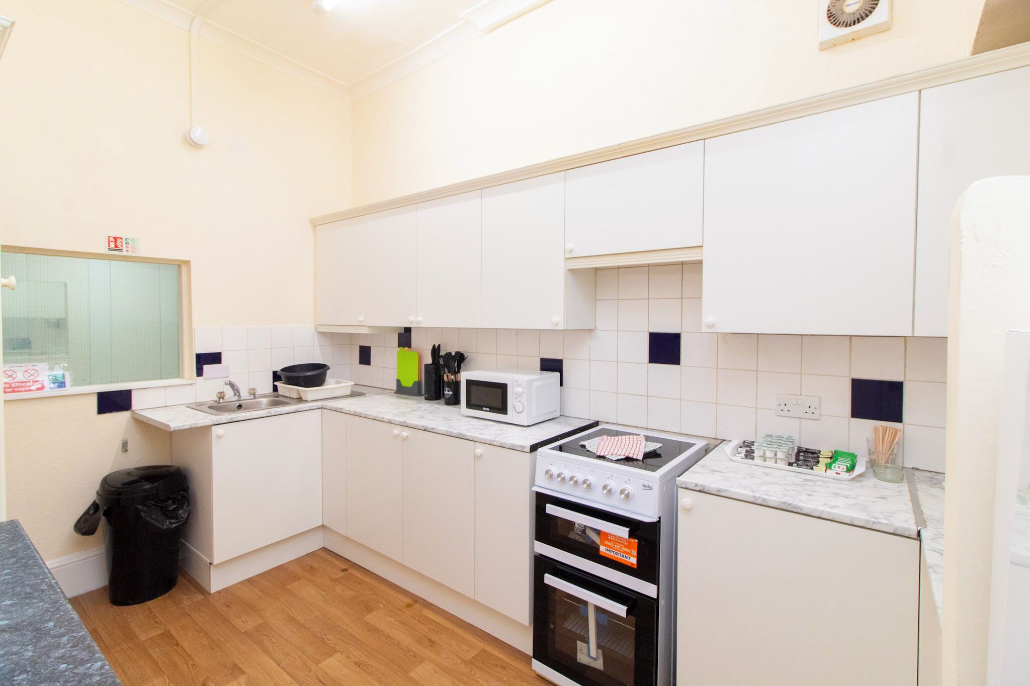 A compact kitchen with white cabinets, a microwave, a stove, and a trash bin.