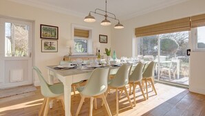 A dining area with a table set for six, surrounded by light green chairs, a chandelier, and framed pictures on the walls. - Fabulous Seaside Retreat (Hunstanton)