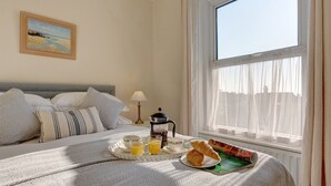 A neatly made bed with pillows, a tray with croissants and orange juice, and a coffee maker on a bedside table. - Fabulous Seaside Retreat (Hunstanton)