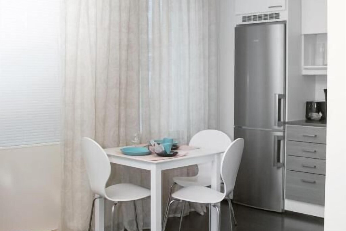 Una habitación moderna y compacta con una mesa de comedor y sillas, un refrigerador y una cama.