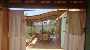 An outdoor patio with a table and chairs, a thatched roof, and a view of the surrounding landscape.