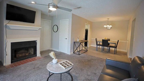 A living room with a fireplace, a ceiling fan, a flat-screen TV, a dining area with a table and chairs, and a sofa.