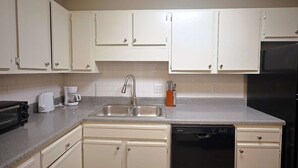 A kitchen with white cabinets, a stainless steel sink, a dishwasher, a toaster, and a coffee maker.
