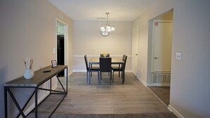 A dining area with a table and chairs, a bench, a vase with dried plants, and a ceiling light fixture.