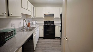 A compact kitchen with white cabinets, a black stove, a sink, and a microwave.