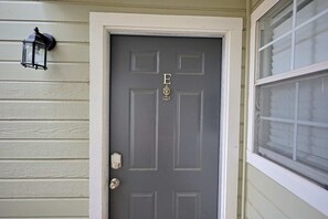 A gray door with the letters "E" and "D" and a trophy symbol, a black lantern on the wall, and a window with blinds.