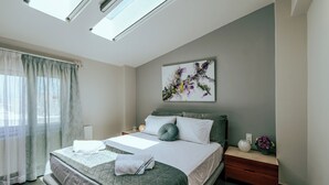 Una habitación de hotel moderna con una cama grande, una mesita de noche, una lámpara de noche, una obra de arte en la pared y una ventana con cortinas translúcidas.