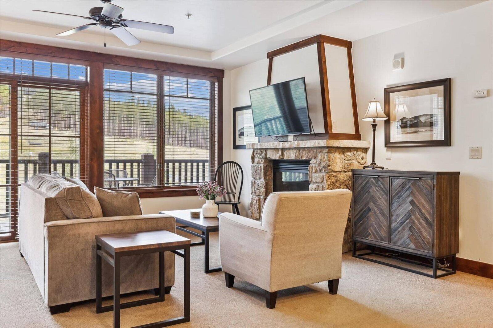 Sala de estar con sofá, sillón y una mesa de centro, una chimenea, televisor montado encima y vistas amplias a través de grandes ventanales.