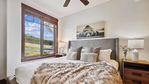 A bedroom with a large bed, a view of a forest through a window, a ceiling fan, and a painting on the wall. - Luxury Crystal Peak Lodge 2 Bedroom Condo - Ski In, Ski Out (Breckenridge)