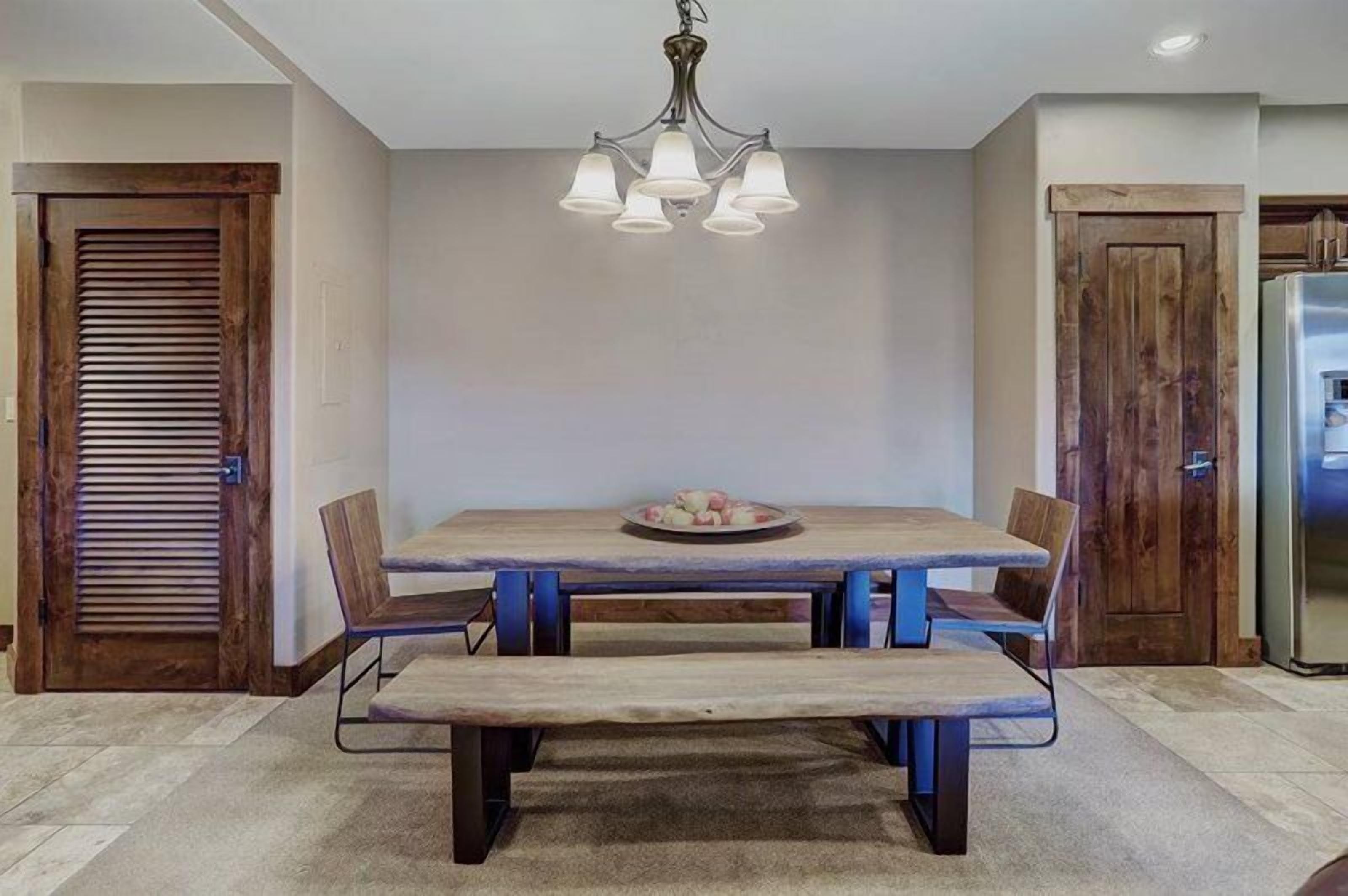 Un espace repas avec une table en bois, des bancs et un lustre.