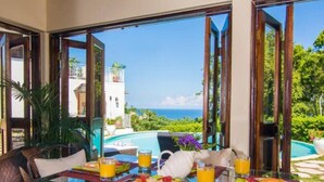 A dining table with breakfast items and drinks, overlooking a pool and a view of a building and the ocean. - Half Hill 3BR (Montego Bay)