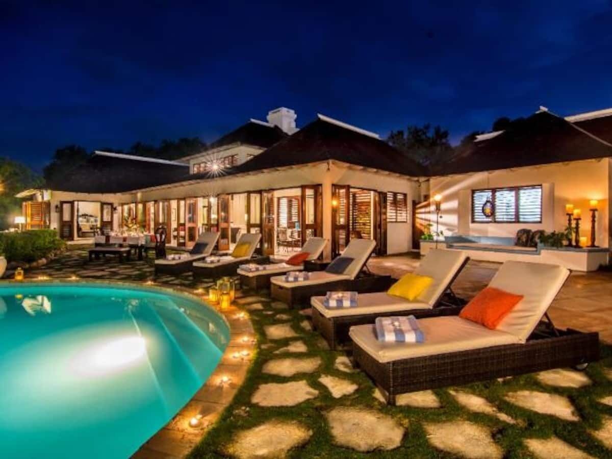 Zona de piscina con sillones de descanso y una alberca, rodeada por un patio bien iluminado con mesas y sillas para comer.