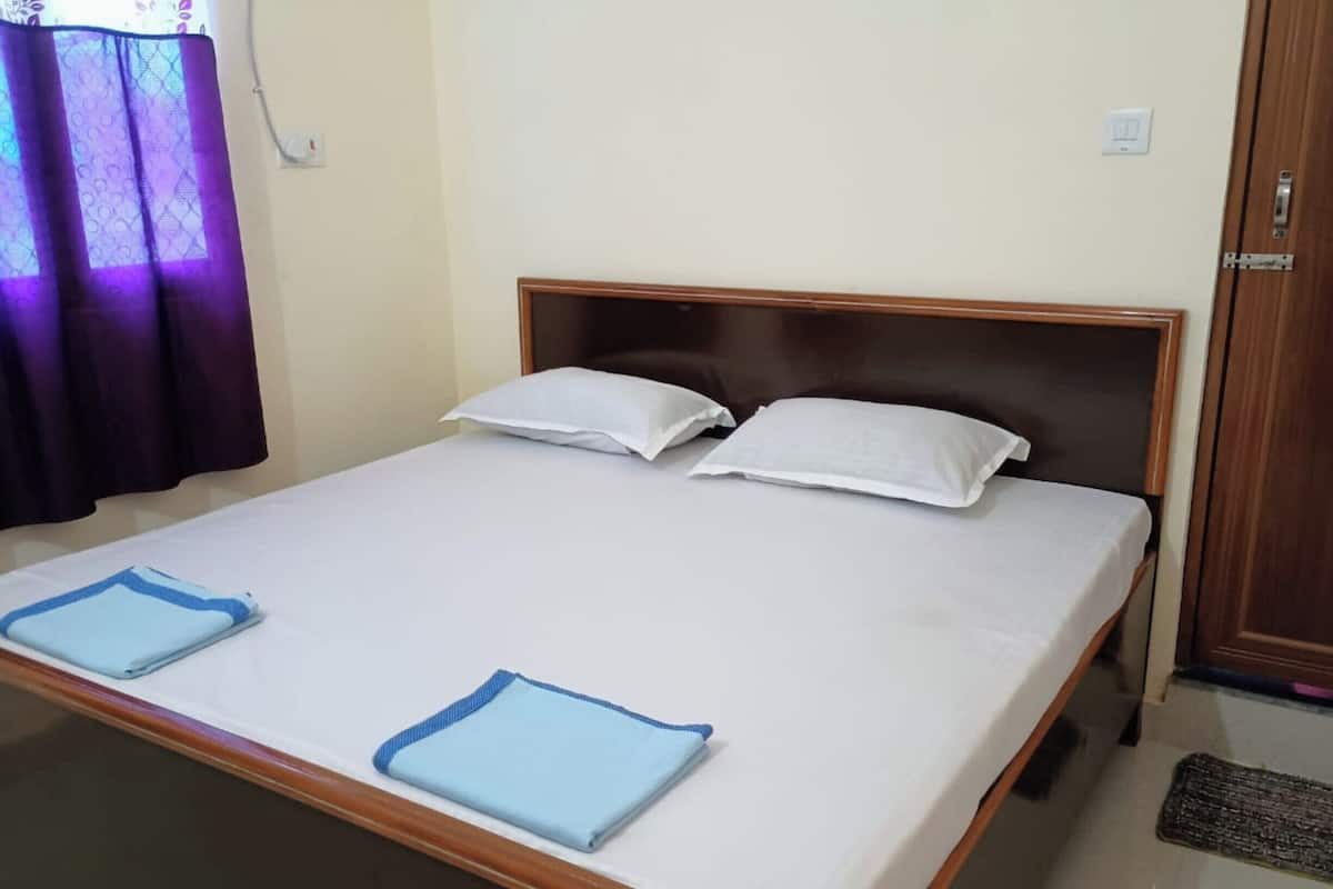 A neatly made bed with white linens and two pillows, a wooden headboard, and a blue towel on the bed.