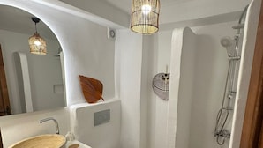 A compact bathroom with a white sink, toilet, and shower. There are decorative items like a woven basket and a wall-mounted shelf. - SelkA Pansiyon (Ayvalik)