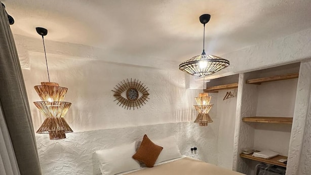 A bedroom with a large bed, two pendant lights, a wall-mounted eye decoration, and a small shelf with folded towels. - SelkA Pansiyon (Ayvalik)