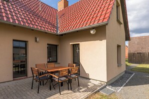 A patio with a table and chairs, a covered outdoor area, and a building with a red-tiled roof.