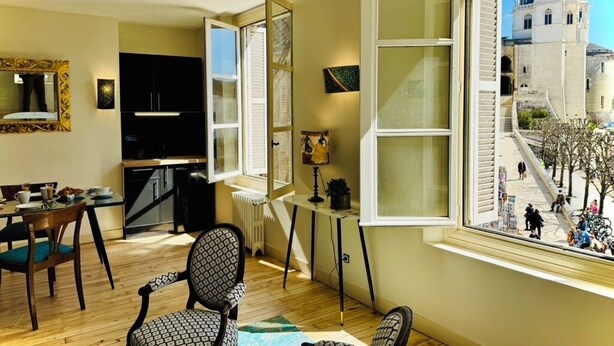 A room with a large window, a dining area with a table and chairs, a black cabinet, and a mirror. - La Chocolaterie, Dream stay, Majestic view of the Chapelle Saint-Hubert (Unknown)