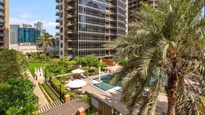 A high-rise building with a pool area, surrounded by greenery and palm trees.