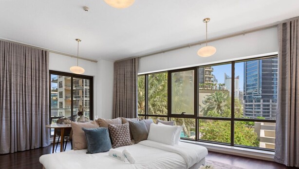 A modern hotel room with a large bed, a dining area, and a view of the cityscape.