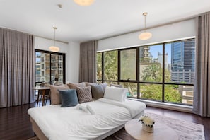 Quarto de hotel moderno com uma cama grande, área de refeições e vista para a cidade.